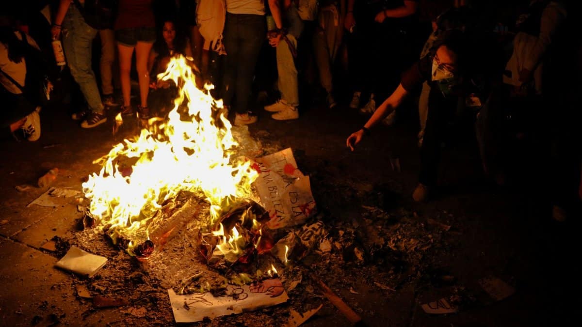 Participants gather around a burning pile of protest signs in Mexico City at night.