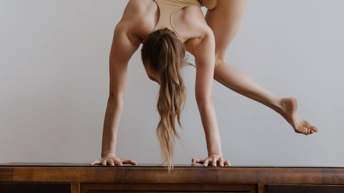 A woman elegantly balances in a handstand on a wooden table, showcasing flexibility and strength.