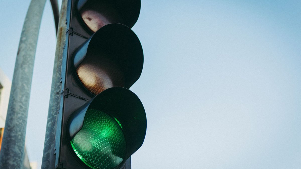 Close-up of a green traffic light against a clear blue sky, symbolizing go and safety.