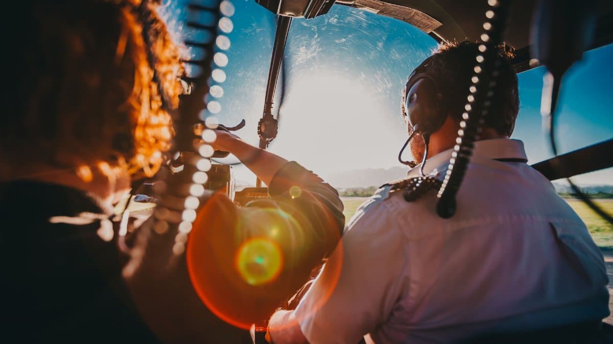 Pilot and passenger view from helicopter cockpit flying over Rio de Janeiro, capturing sun glare.