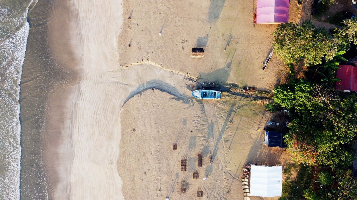 Drone shot captures serene beach scene with a lone boat and pristine white sand.