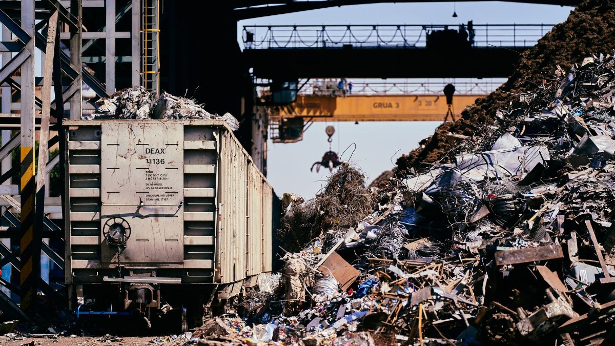 A dynamic industrial scene featuring a scrap yard with a train car and crane lifting debris.