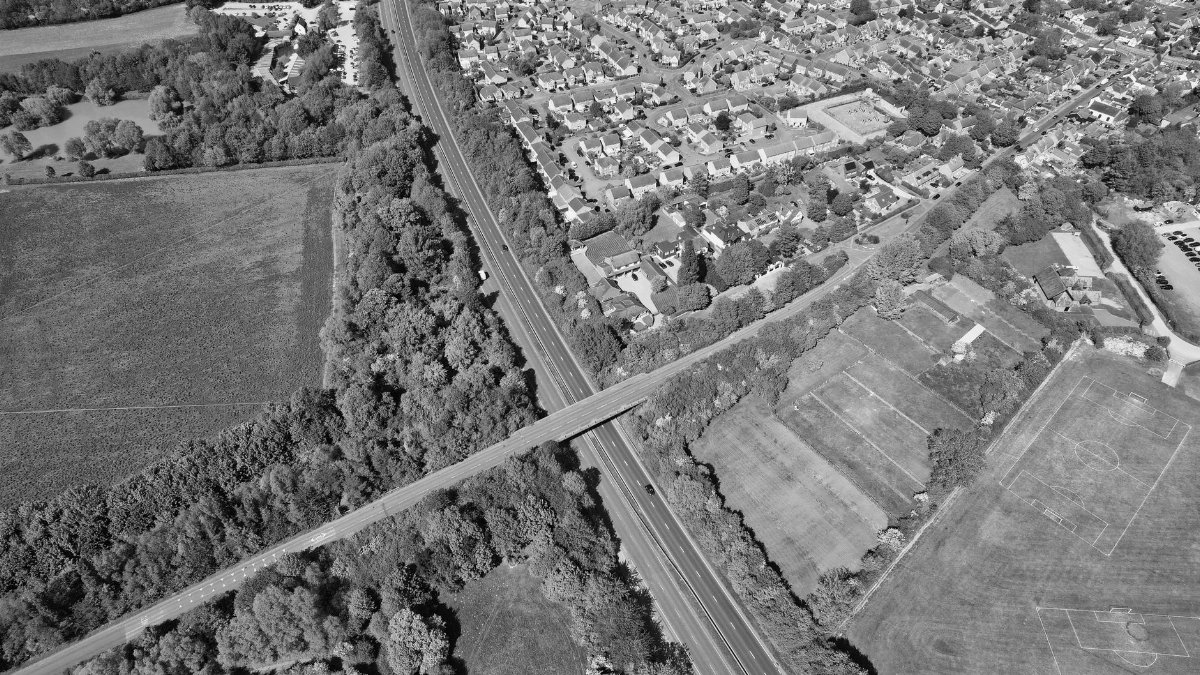 Aerial black and white photo of a town in England with roads, fields, and residential areas.