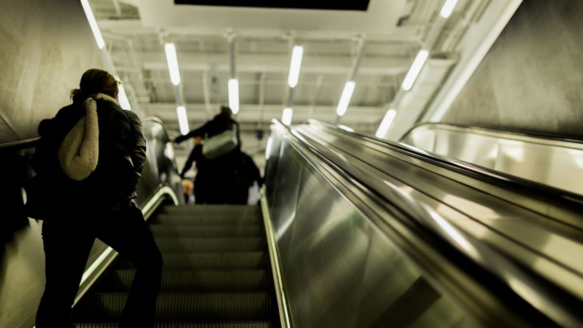 View of an indoor escalator with people moving upwards under bright lights.