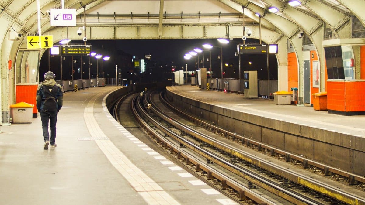 A lone traveler walks through a Berlin subway station at night, featuring bright lights and empty platforms.