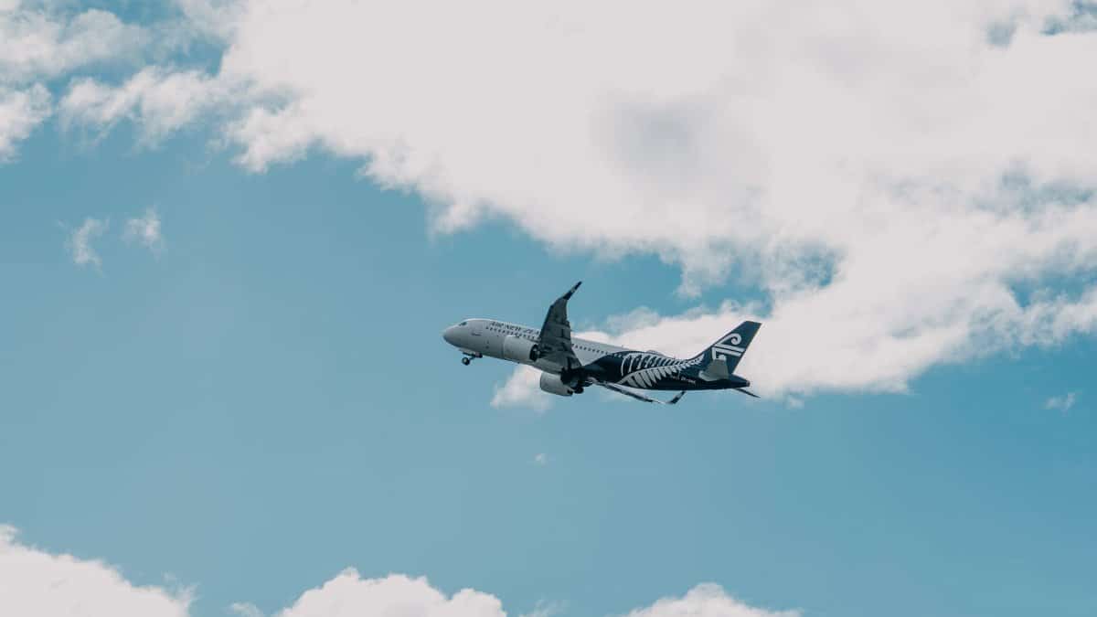 A commercial airplane soaring through a blue sky with fluffy white clouds, capturing a travel scene in New Zealand.