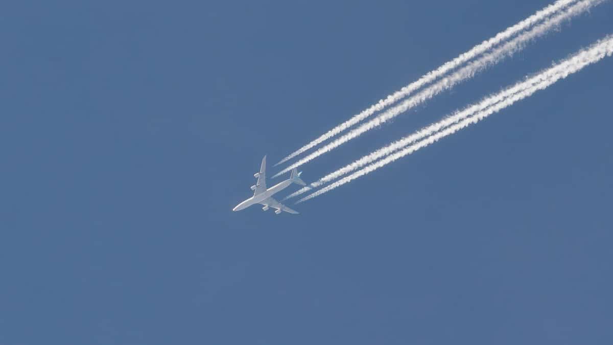 A commercial airplane cruising at high altitude, leaving visible contrails against a clear blue sky.