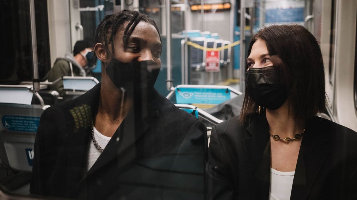 Two people wearing masks sit and converse on a train, illustrating public transit in the pandemic era.