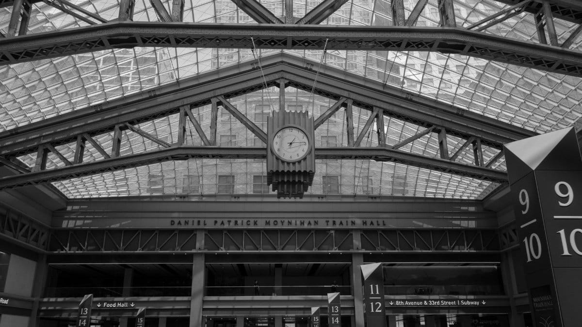 Black and white image of Daniel Patrick Moynihan Train Hall interior with clock and crowd.