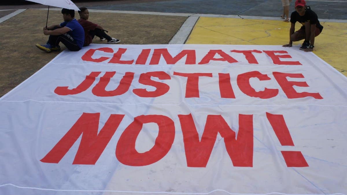 Large protest banner reading 'Climate Justice Now!' displayed outdoors during a demonstration.