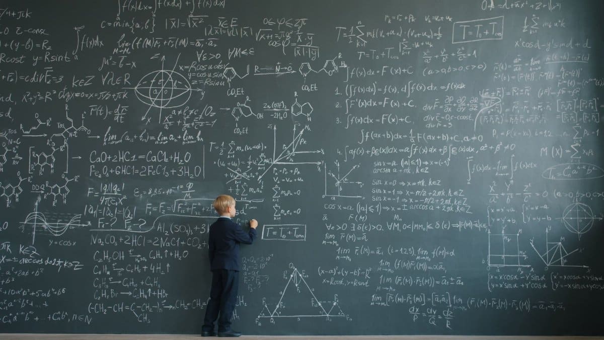A young student solving complex math equations on a classroom chalkboard.
