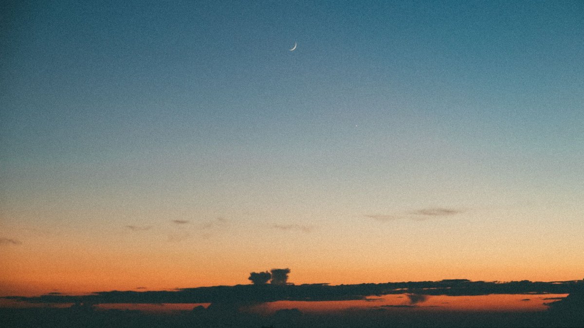 A tranquil twilight sky with a crescent moon over a calm ocean, capturing the serene beauty of nature.
