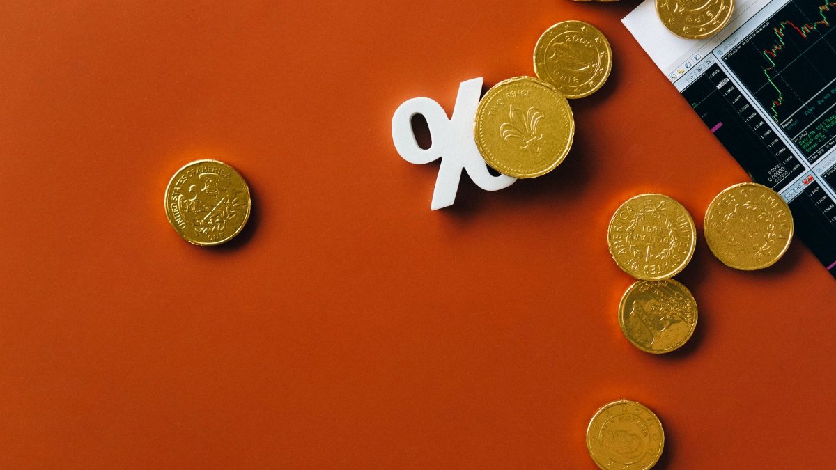 Gold coins scattered with a stock market graph and a percentage symbol on an orange background.