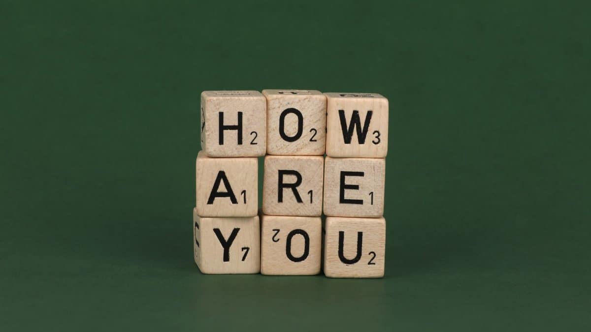 Wooden Scrabble letter blocks spelling 'how are you' on a green background.