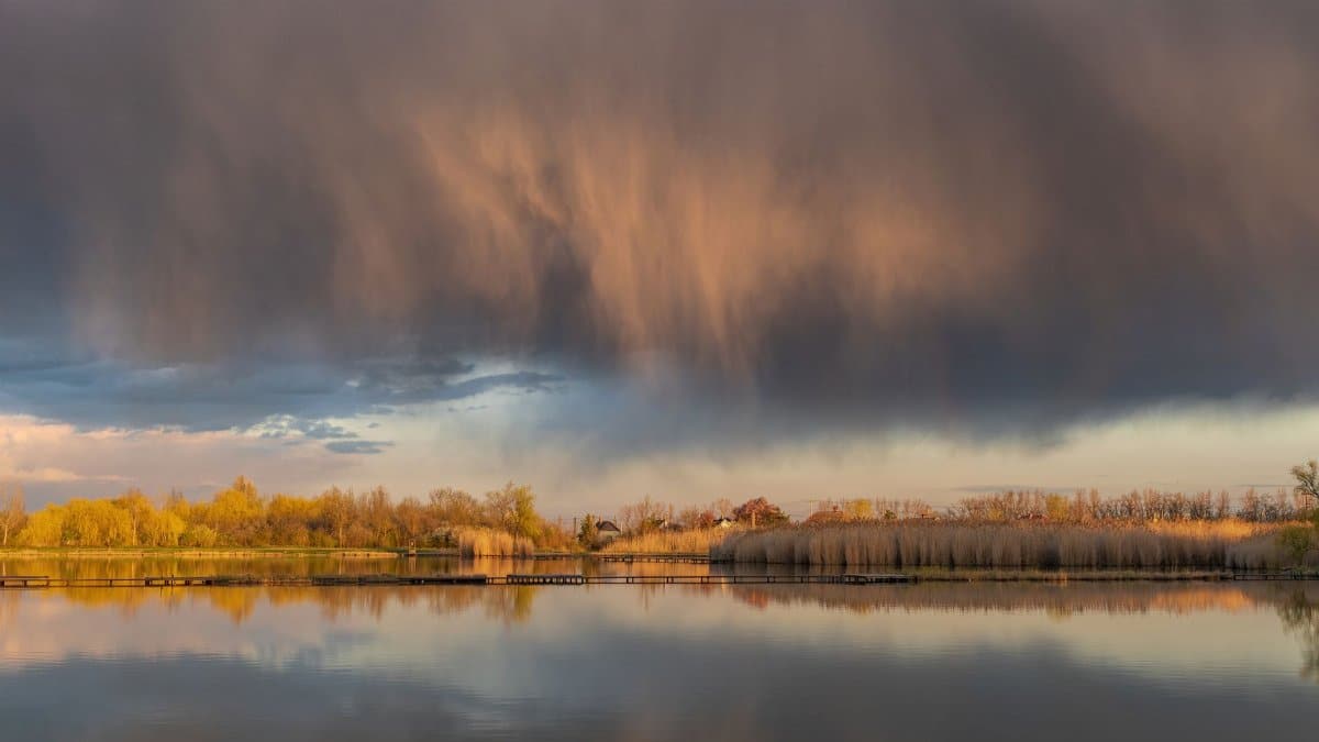 Autumn lake landscape with dramatic storm clouds casting reflections on the water.