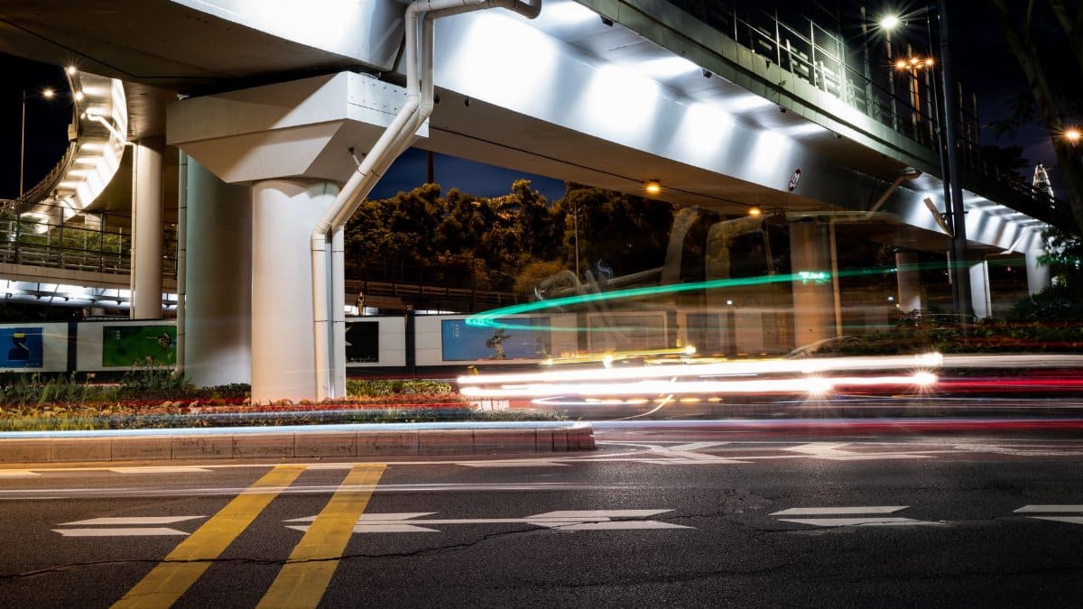 A vibrant nighttime city street with dynamic light trails beneath an illuminated overpass.