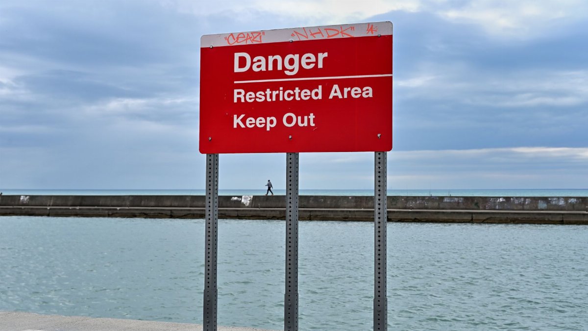 A vivid red danger sign warns to keep out at Lake Michigan's edge under cloudy skies.