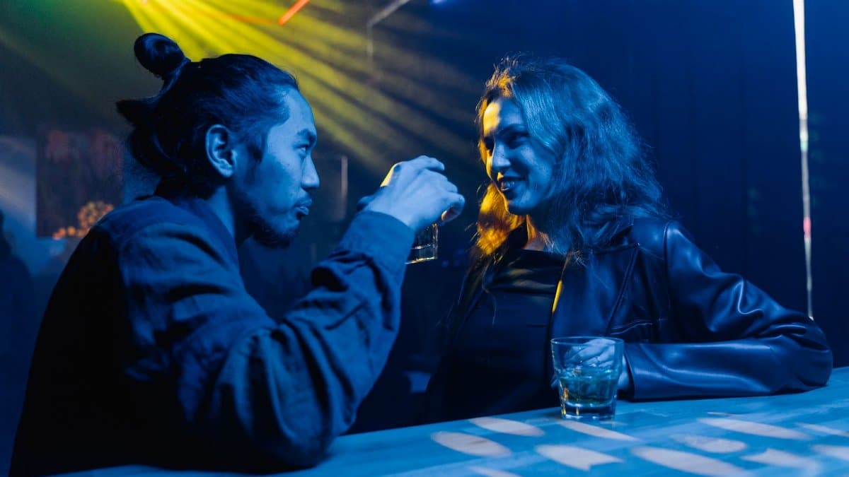 A man and a woman conversing in a vibrant nightclub, sharing drinks under colorful lights.