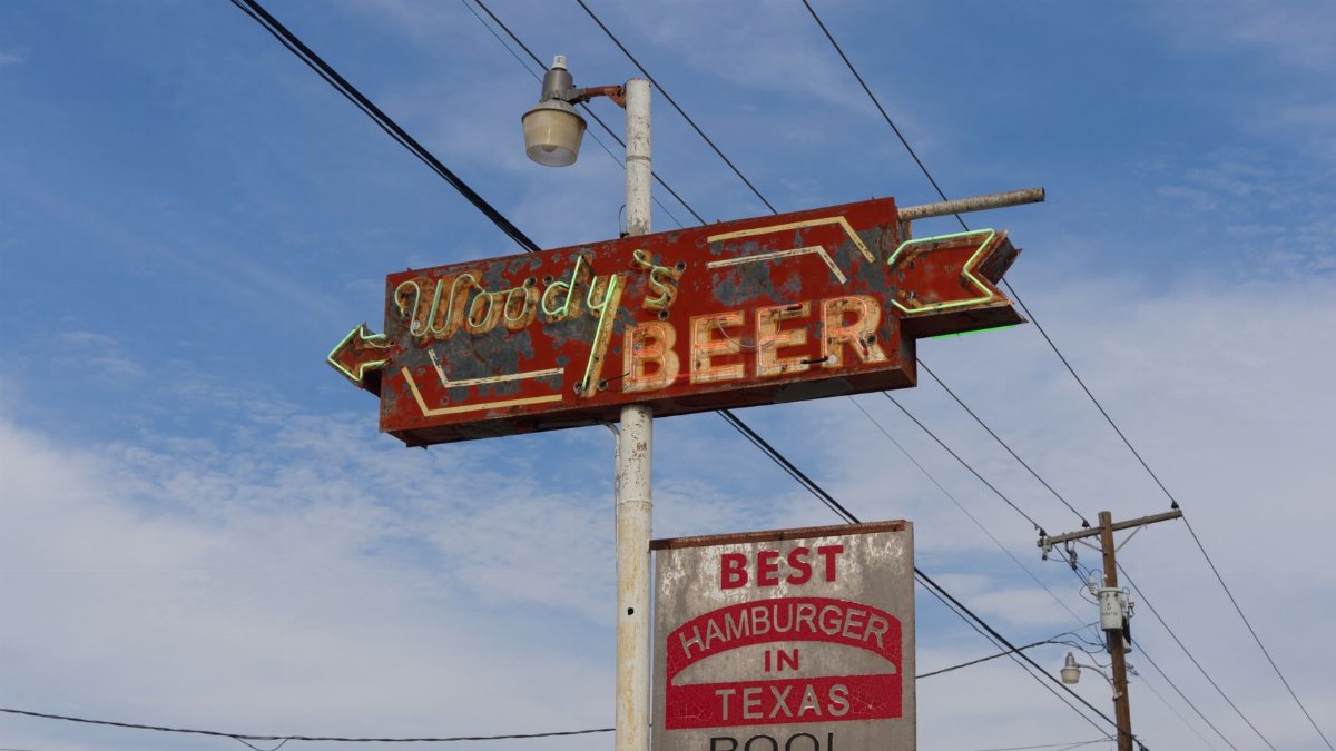 Rusty vintage Woody's Beer sign against a clear blue sky in Mineral Wells, Texas.