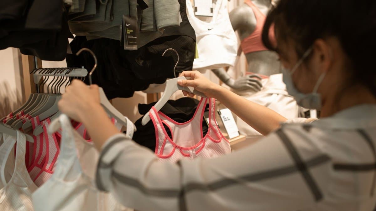 A woman wearing a face mask shops for sports bras in a store, highlighting new normal shopping experience.