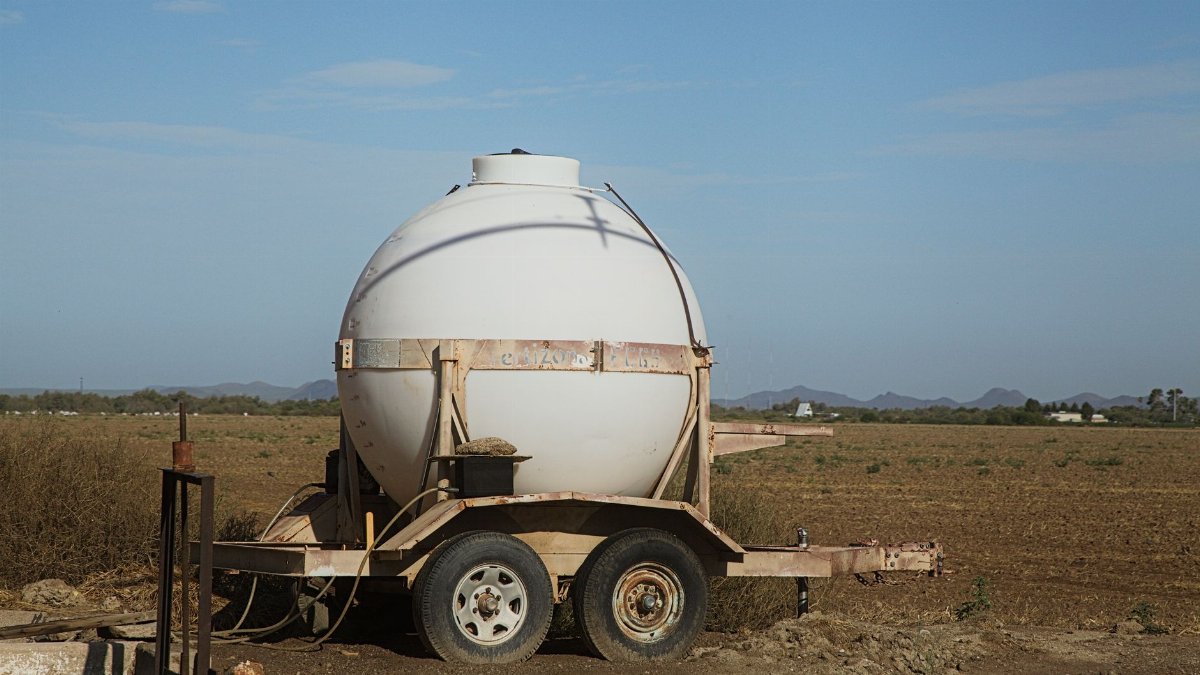 A round water tank on a trailer set in a rural field under a clear blue sky.