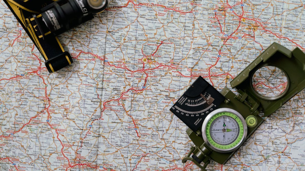 Overhead view of a map with a compass and flashlight showing navigation tools.