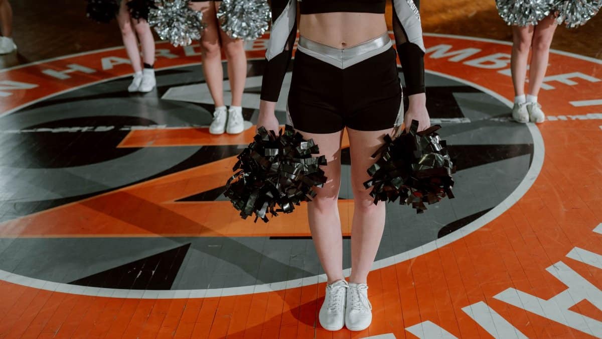 Cheerleading team in formation with pom-poms on an indoor basketball court, ready for performance.