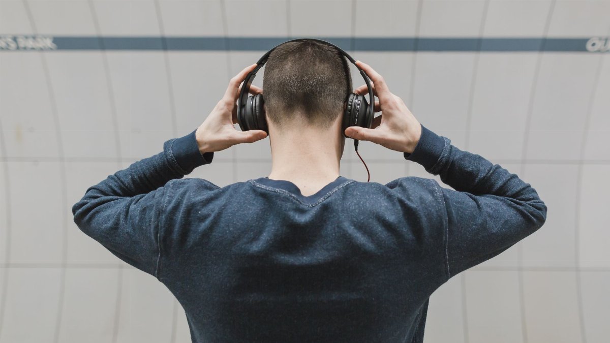 Man with headphones listening to music indoors, wearing long sleeves. Back view shot.