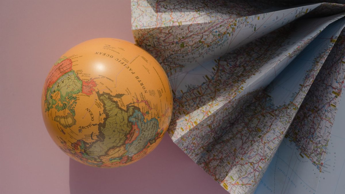 A globe and a folded map on a pink background, showcasing geography and cartography.