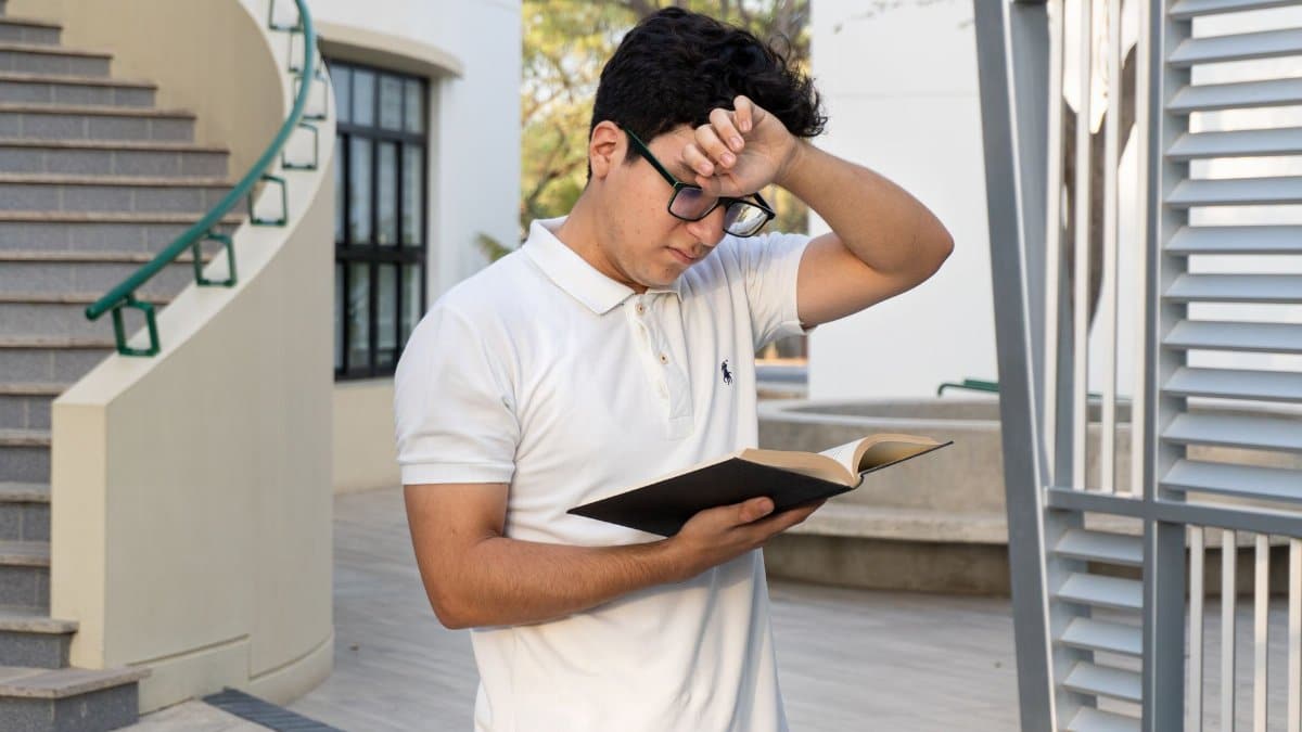 A young man in a white polo reads a book outdoors in a modern setting in Piura, Peru.