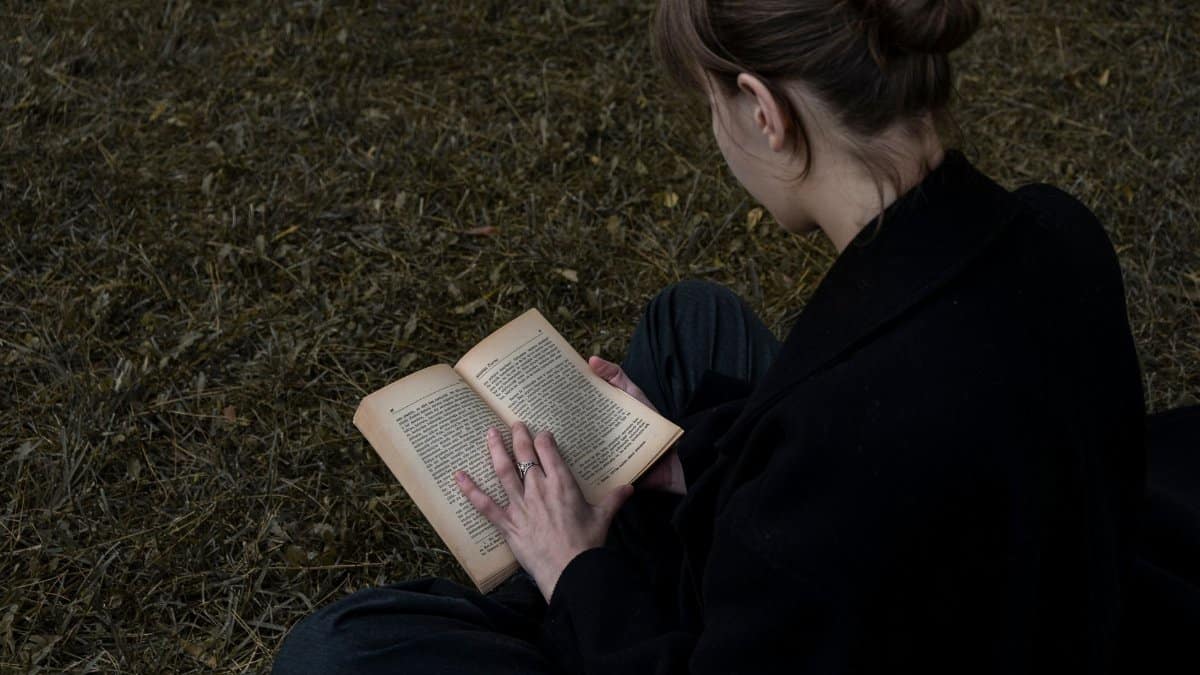 A young woman sits in an outdoor area reading a book, showcasing a peaceful moment of literature in nature.
