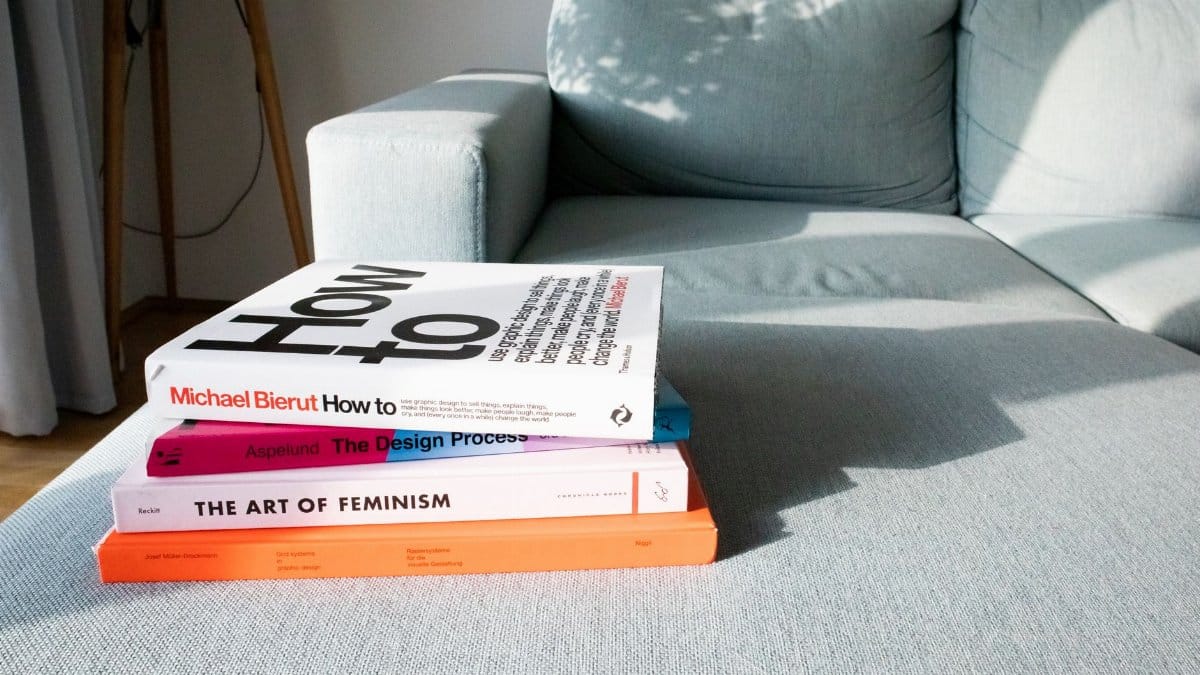 Close-up of design and art books on a modern sofa in a sunlit living room.