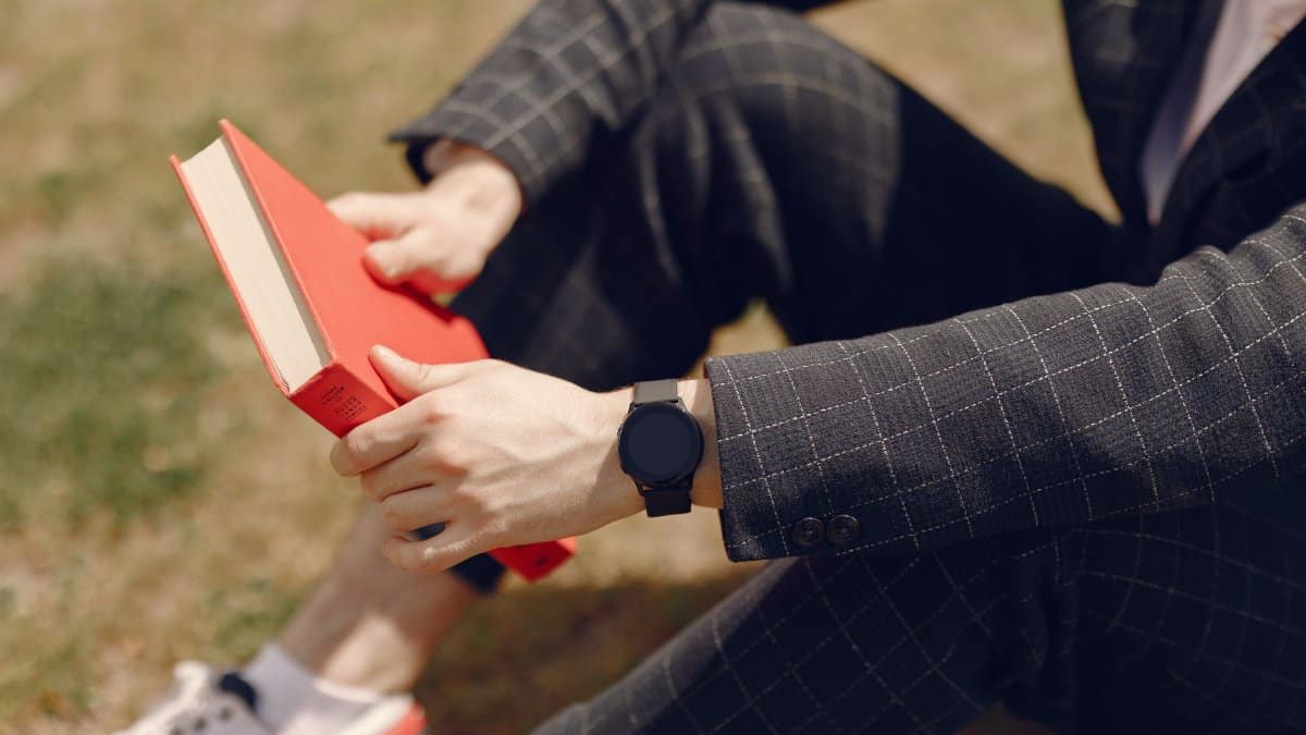 Stylish man in suit reading a red book outdoors on a sunny day.