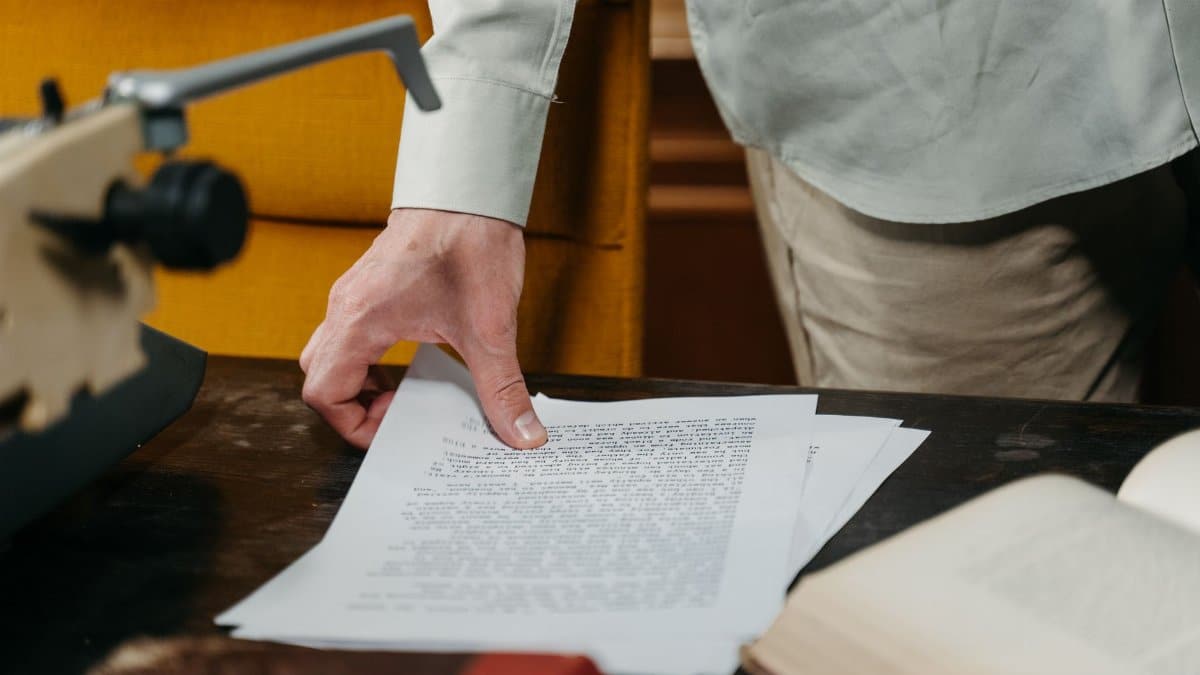 Close-up of a hand reaching for a document on a desk with a typewriter and book.