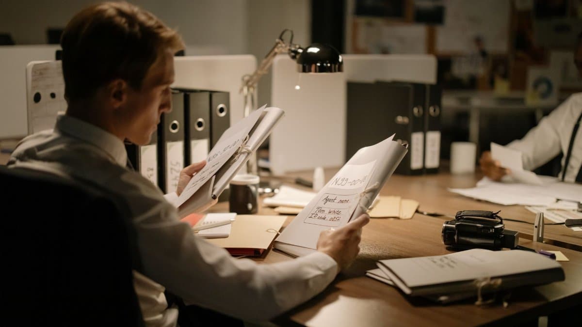 Two detectives reviewing documents in a dimly lit office setting, focused and professional.