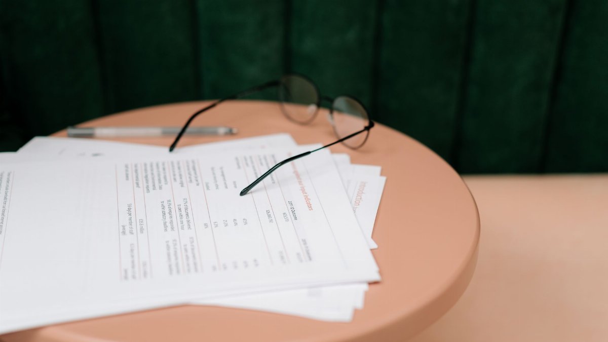 A close-up of documents, eyeglasses, and a pen on a round table indoors.