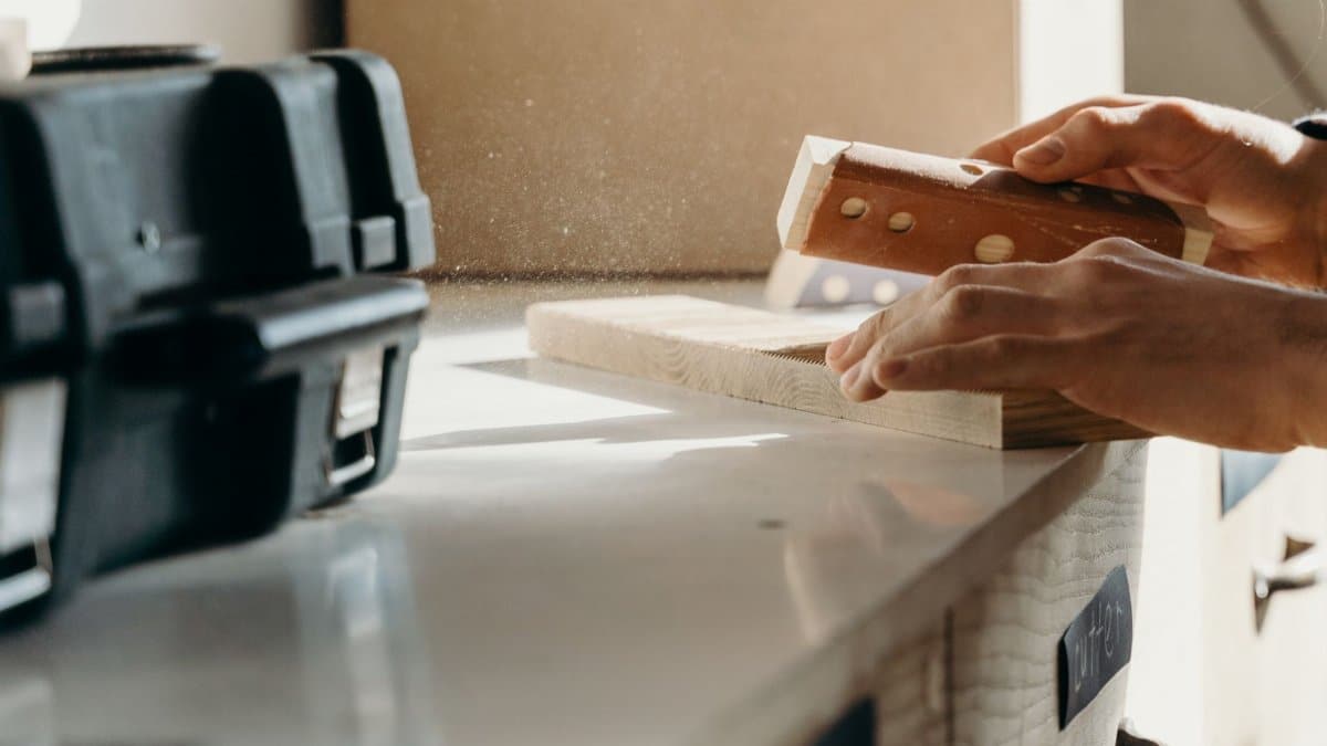 Detailed shot of hands sanding wood with care, showcasing craftsmanship in a workshop setting.