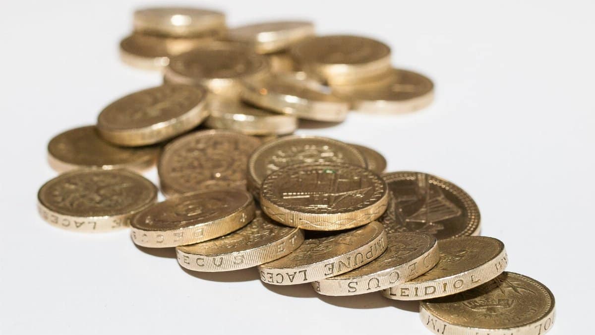 Close-up of assorted British pound coins scattered on a white surface, highlighting financial themes.