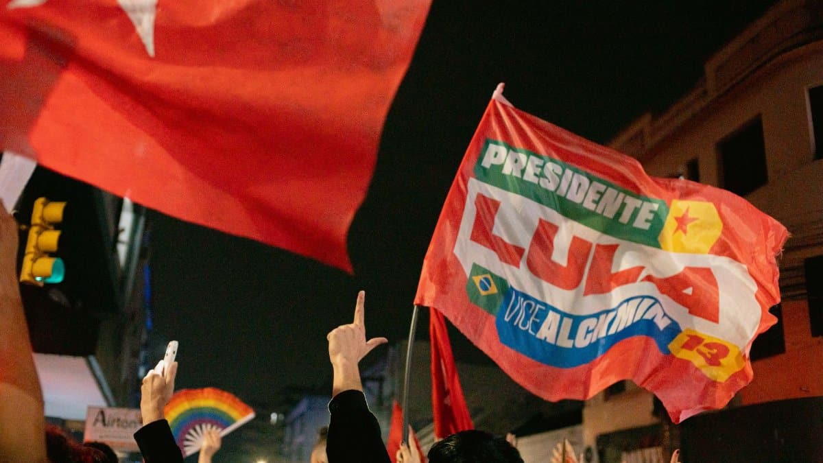Supporters at a night rally waving flags with political slogans and hand signs.