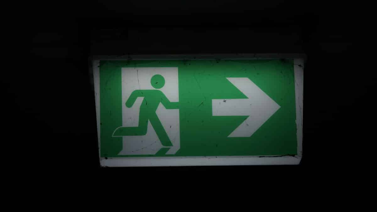 Illuminated green emergency exit sign with an arrow pointing right in a dark setting.