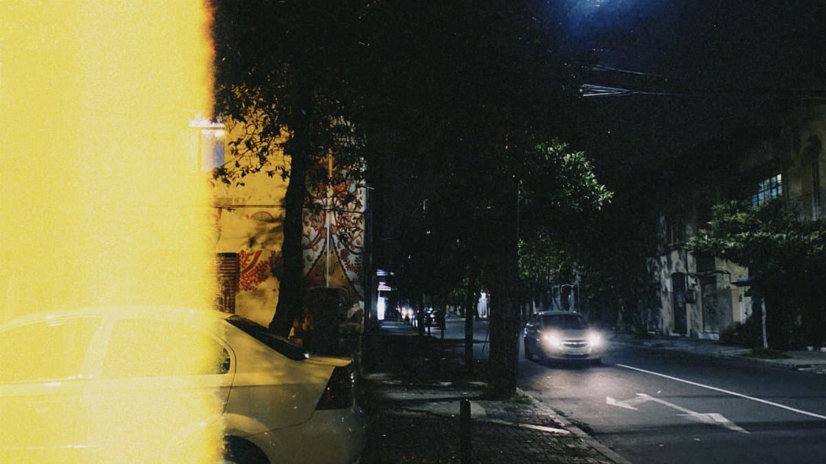 Street view of a city at night with cars and dramatic lighting, creating a moody, urban atmosphere.
