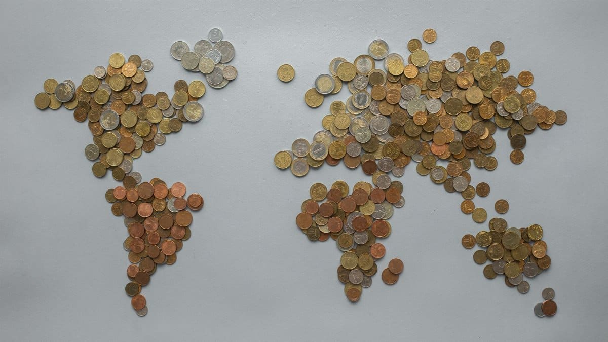 Creative world map made from assorted coins on a solid gray backdrop, symbolizing global finance.
