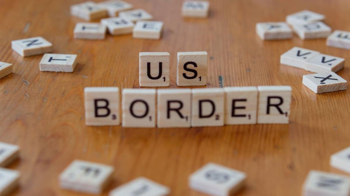 Scrabble tiles spelling 'US Border' on a wooden surface, symbolizing immigration themes.