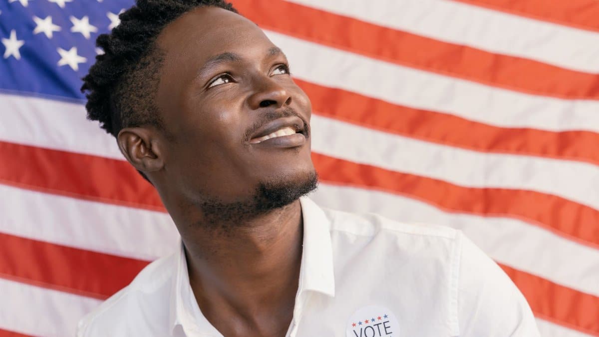 Man smiling with a voting sticker against an American flag background, symbolizing patriotism.