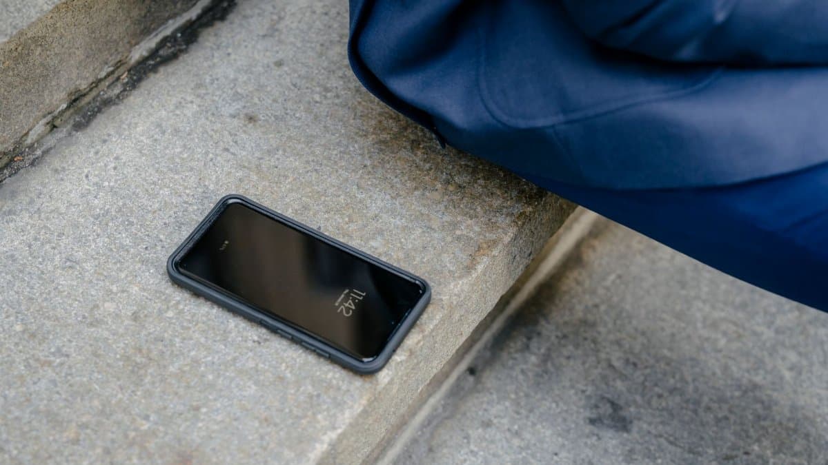 A smartphone is left unattended on concrete steps outdoors, next to a person in blue clothing.