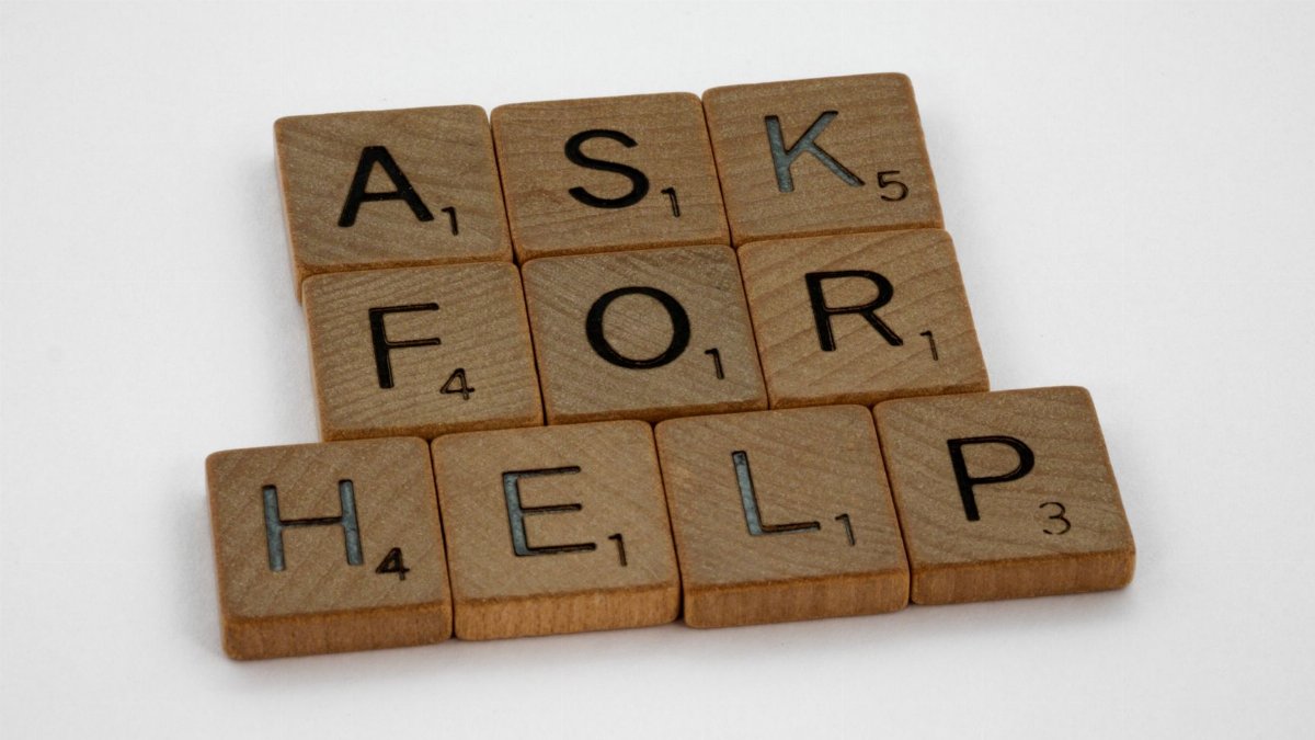 Wooden Scrabble tiles on a white surface spelling 'Ask for Help' in a conceptual layout.