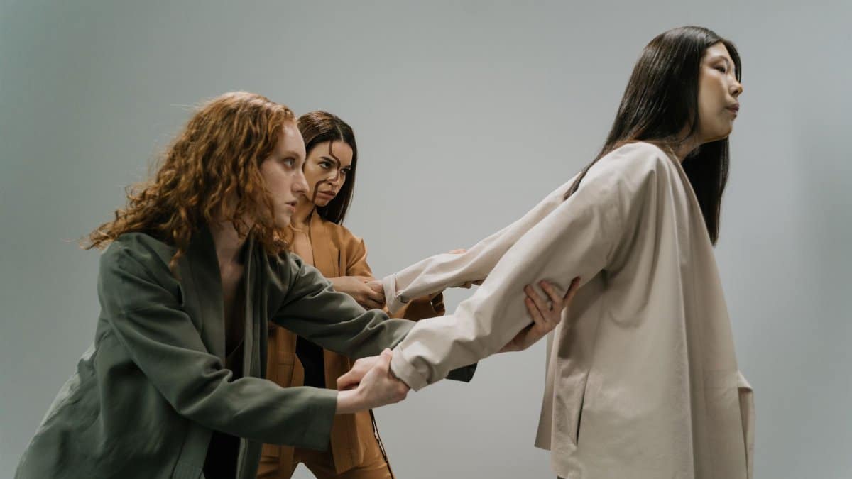 Three women in a conceptual studio shoot conveying struggle and connection.