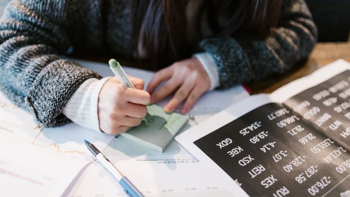 Close-up of a person writing on a sticky note amidst documents in an office setting.