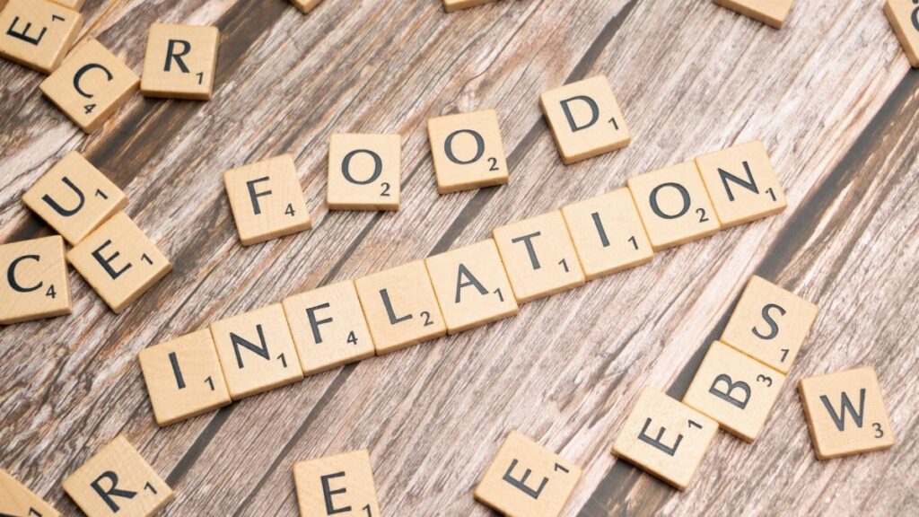 Wooden scrabble tiles arrange to spell 'Food Inflation' on a rustic wooden surface, conceptually depicting rising food prices.