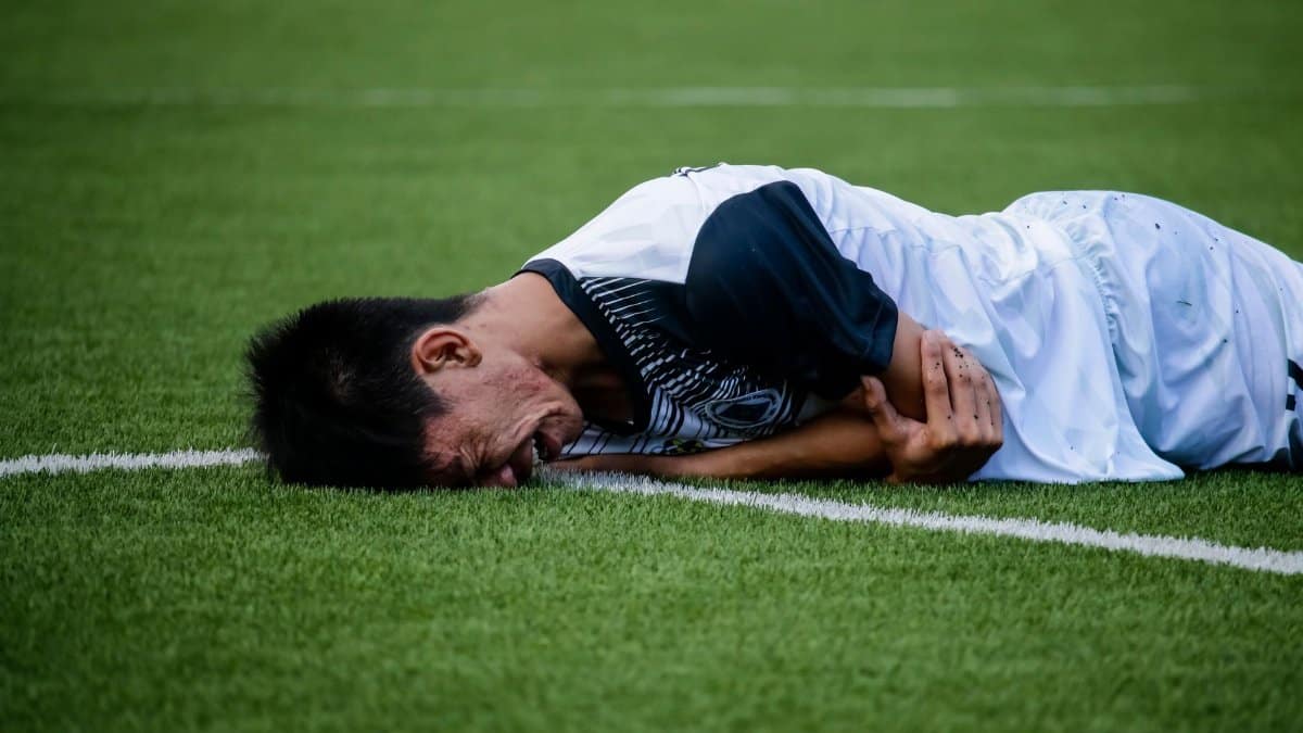Soccer player lies on the field in pain during a game, indicating possible injury.